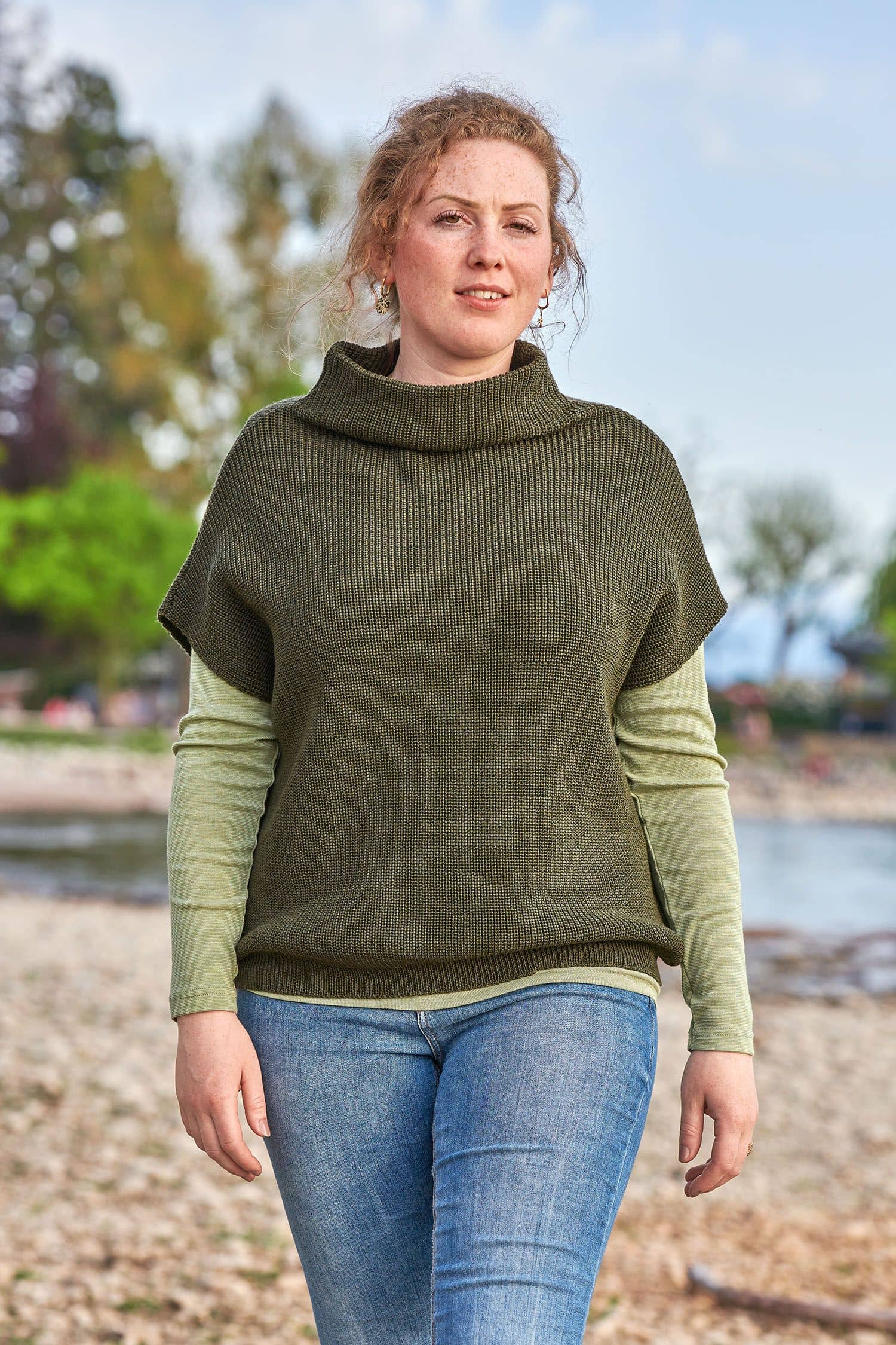 Frau trägt olivegrünen Strickpullunder aus bio Wolle (kbT) vom Finkhof mit grünem Shirt und Jeans