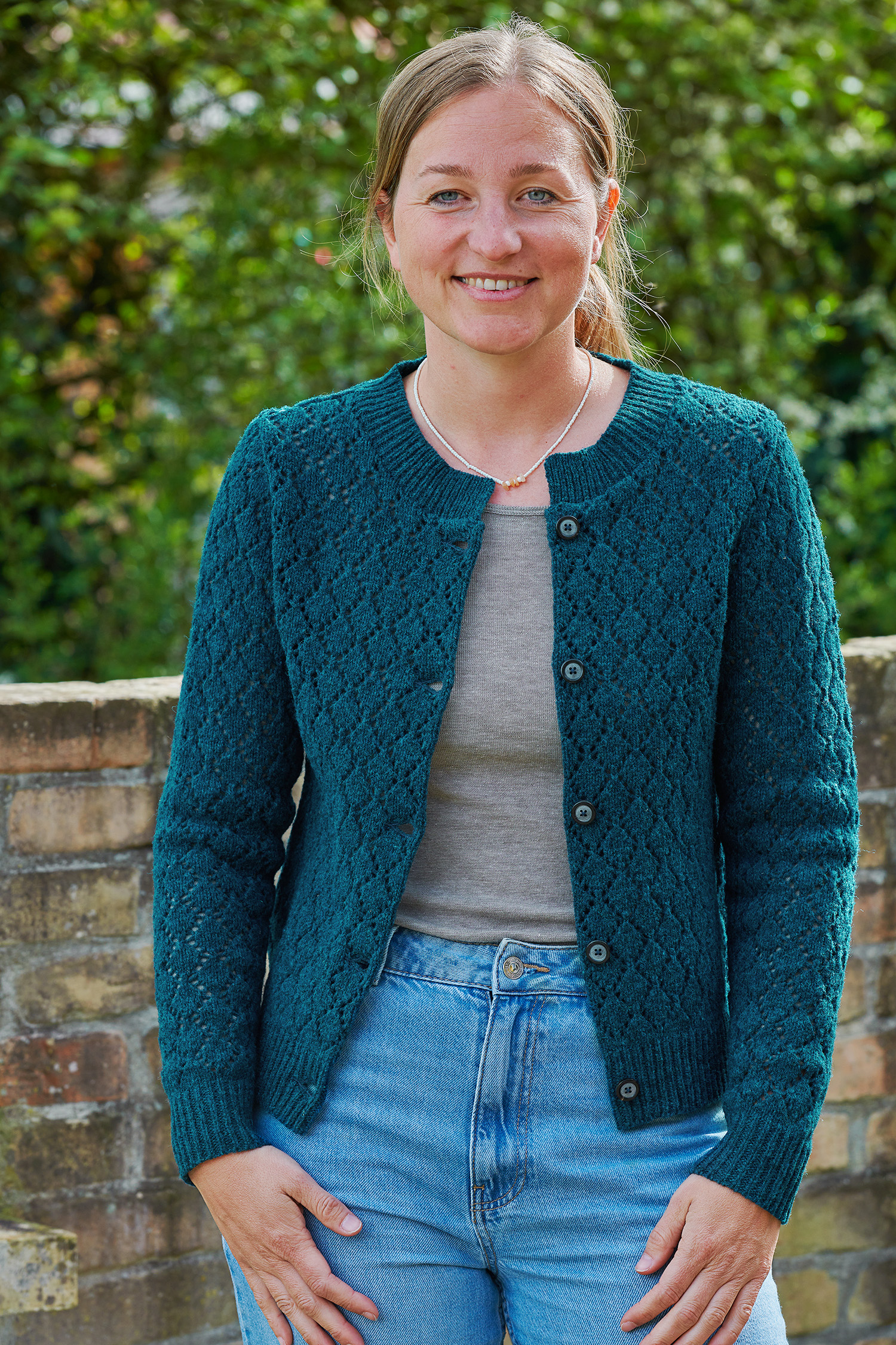 Frau trägt blaues Shirt, eine weite helle Hose und eine blaue Weste mit Ajourmuster vom Finkhof