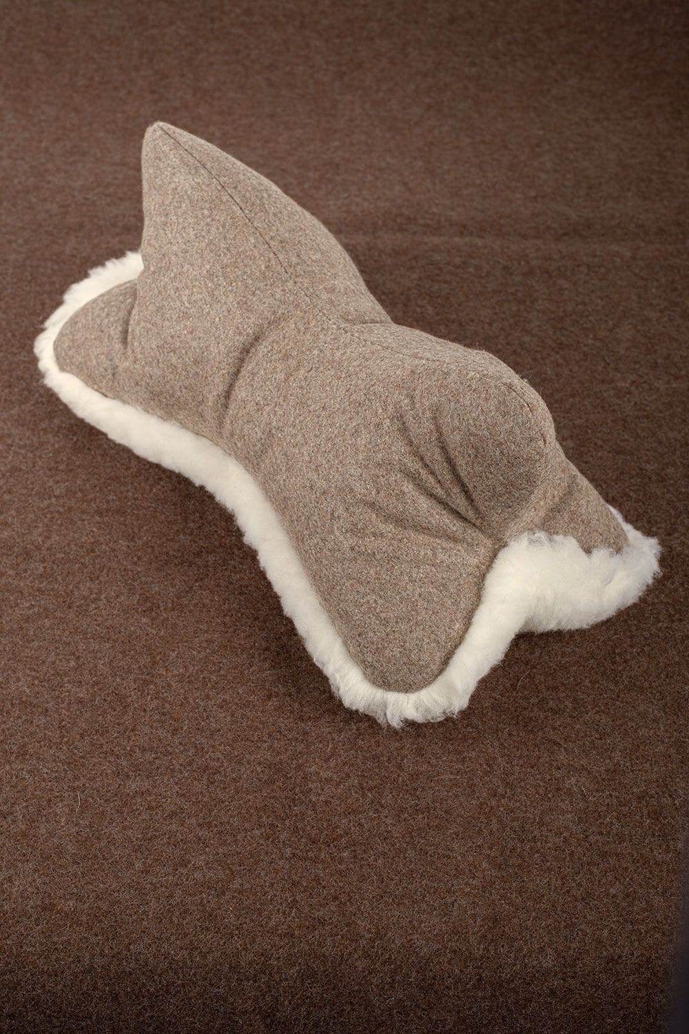 Finkhof Leseknochen aus Schaffell, Loden und Rohwolle (kbT) liegt auf braunem Untergrund, Fell liegt nach unten