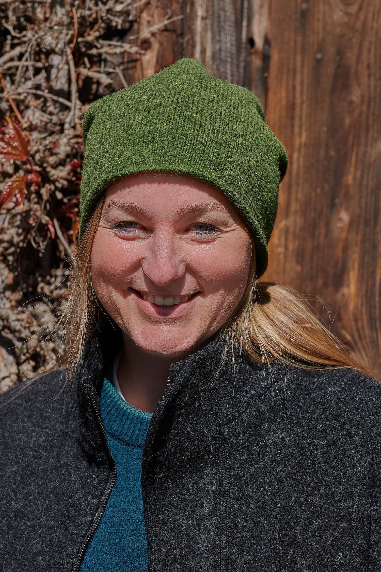 Frau trägt eine grüne Strickmütze vom Finkhof aus Bio-Wolle, einen türkisen Pulli und eine schwarze Jacke