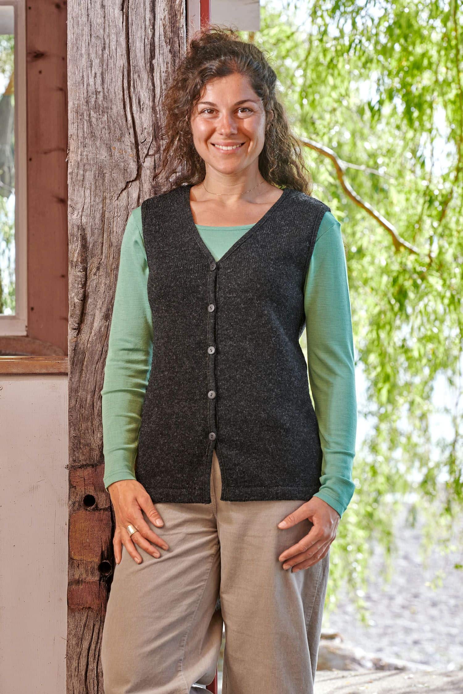 Frau trägt eine graue Strickweste ohne Ärmel aus bio Wolle (kbT) vom Finkhof mit grünem Shirt und beiger Hose