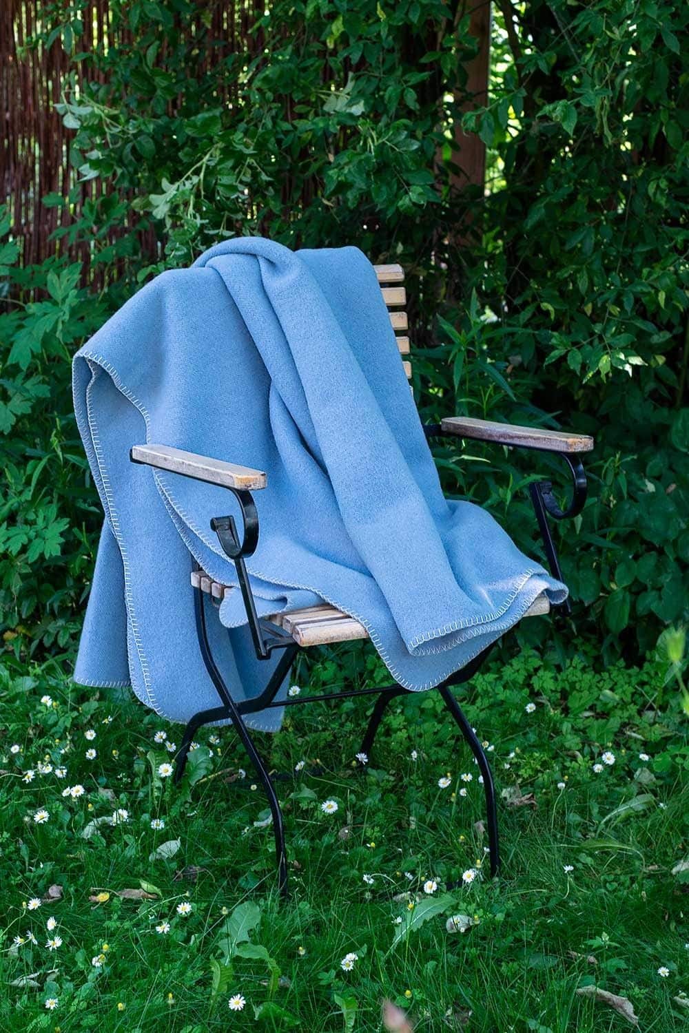 hellblaue Wolldecke aus bio Wolle (kbT) vom Finkhof hängt über einem Gartenstuhl