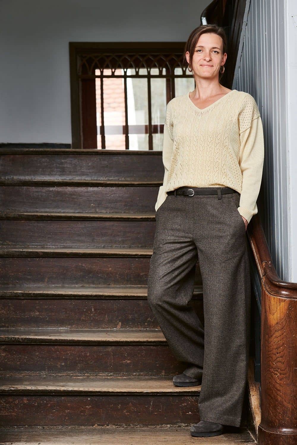 Frau steht auf Treppe und trägt weißen Pulli und eine braunmelierte Wollhose aus bio Wolle (kbT) vom Finkhof