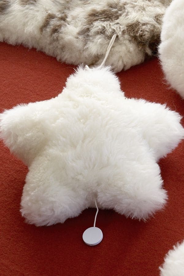 weiße Finkhof Spieluhr in Sternenform aus Fell und bio Wolle (kbT) auf rotem Untergrund