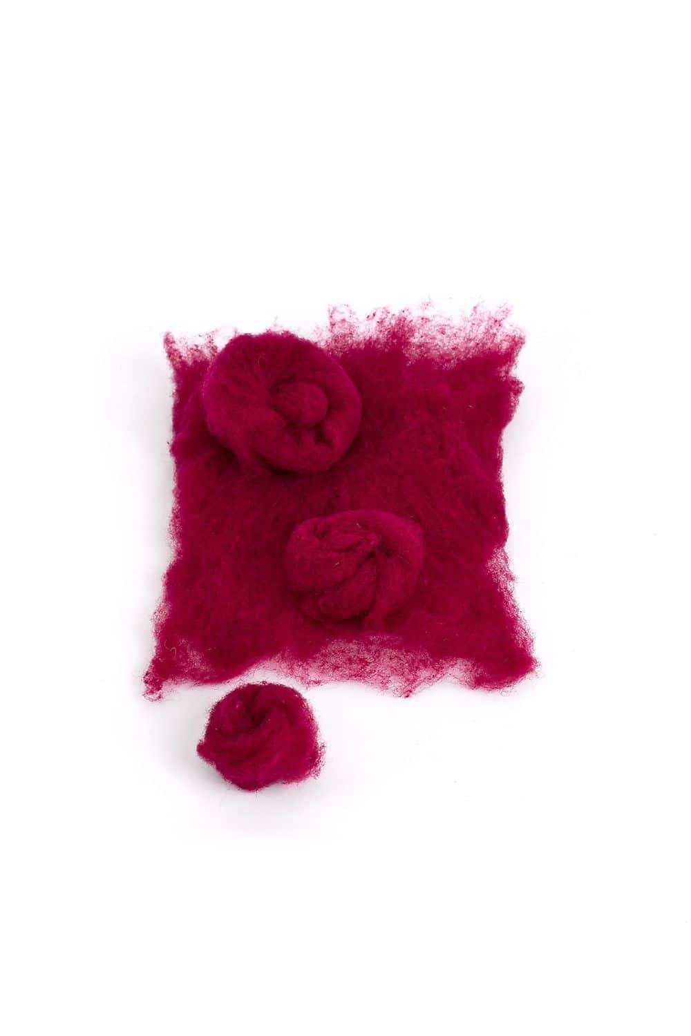 Stück lose rote Finkhof Märchenwolle aus bio Merinowolle (kbT) und rote Filzkugeln auf weißem Untergrund