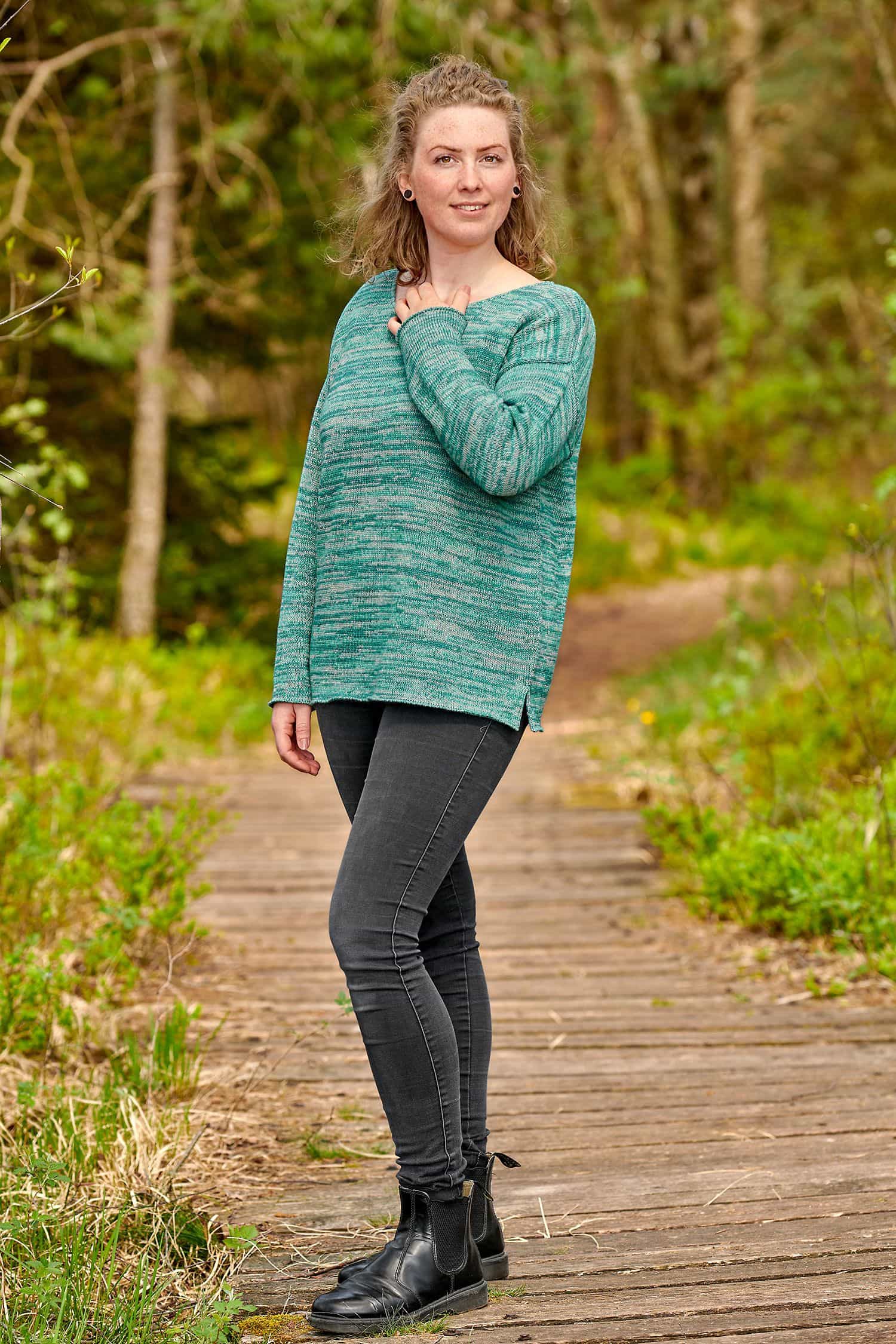 Frau trägt einen türkismelierten oversize Strickpullover aus bio Baumwolle (kbA) und bio Wolle (kbT) und eine schwarze Jeans