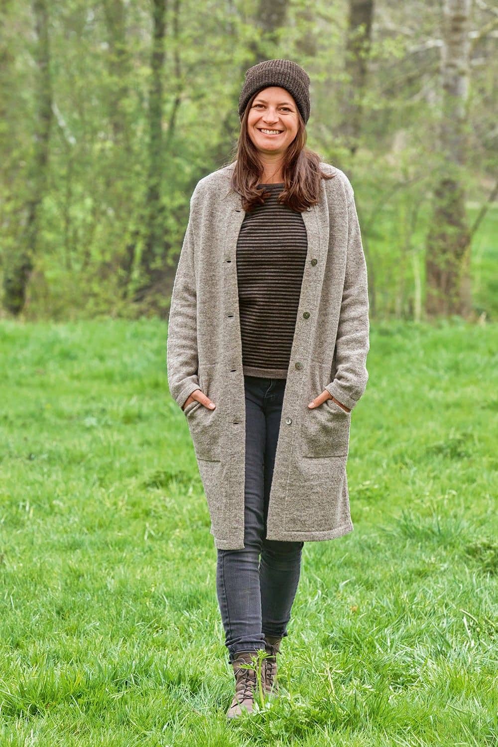 Finkhof-Strickmantel grau Gr. M Frau auf Wiese trägt grauen offenen Finkhof Strickmantel aus bio Wolle (kbT) mit Mütze, Streifenshirt und Jeans