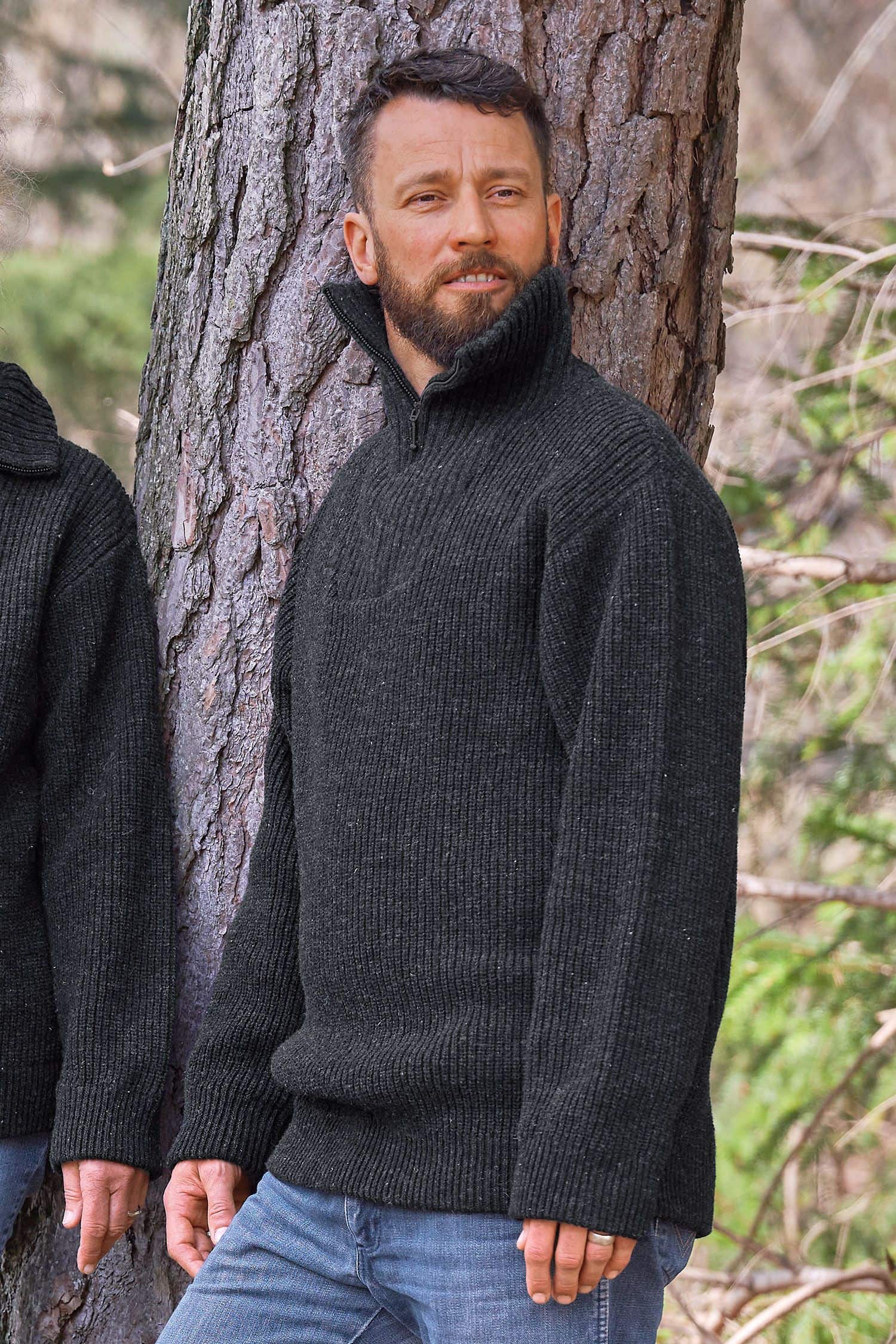 Mann mit Jeans steht neben Baum und trägt anthraziten Finkhof Troyer mit Zipper aus bio Wolle (kbT)