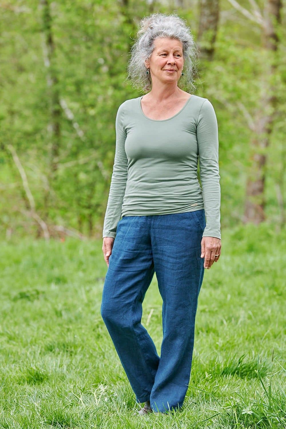 Frau steht im Grünen und trägt eine Jeans mit schilfgrünem Langarmshirt aus bio Baumwolle (kbA) und Elasthan