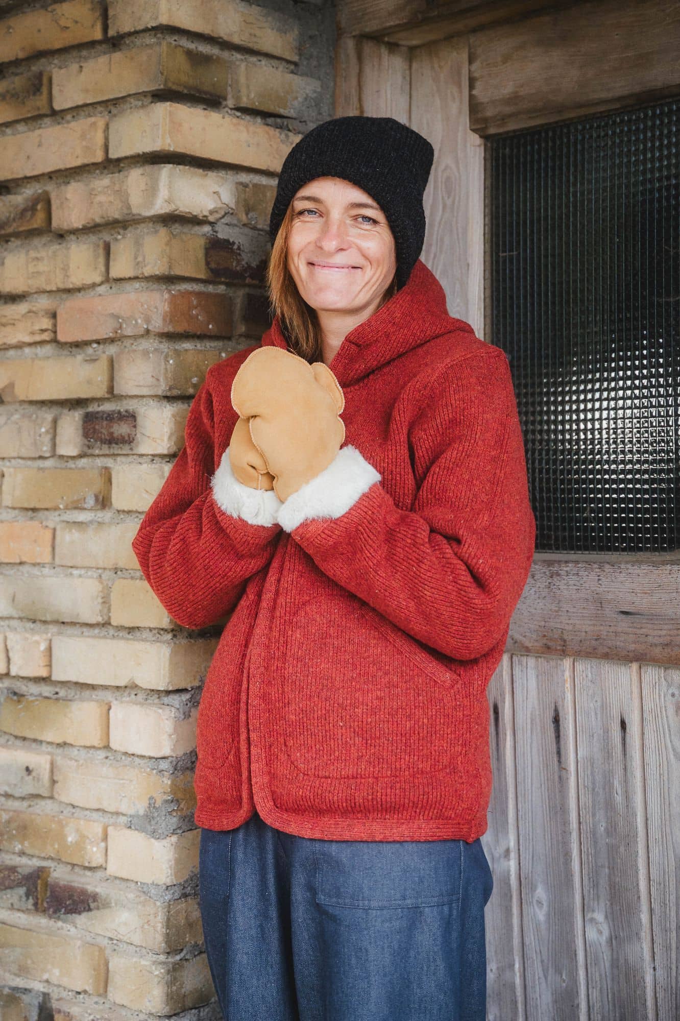 Frau mit braunen Handschuhen und Mütze trägt eine rote Wollwalk Kapuzenjacke aus bio Wolle (kbT) vom Finkhof