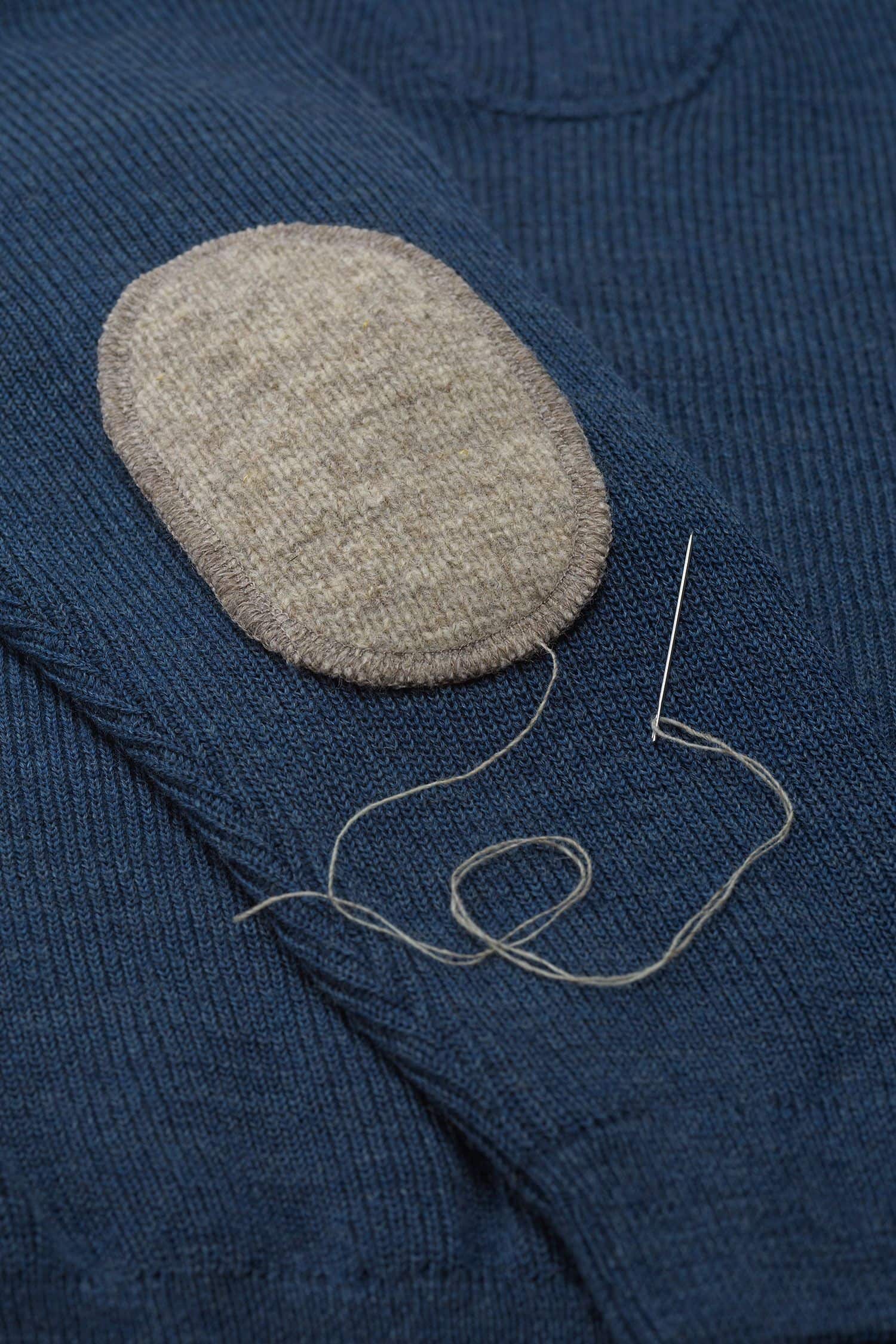 grauer Ellenbogenpatch aus bio Wolle (kbT) vom Finkhof wird auf blauen Pulli genäht