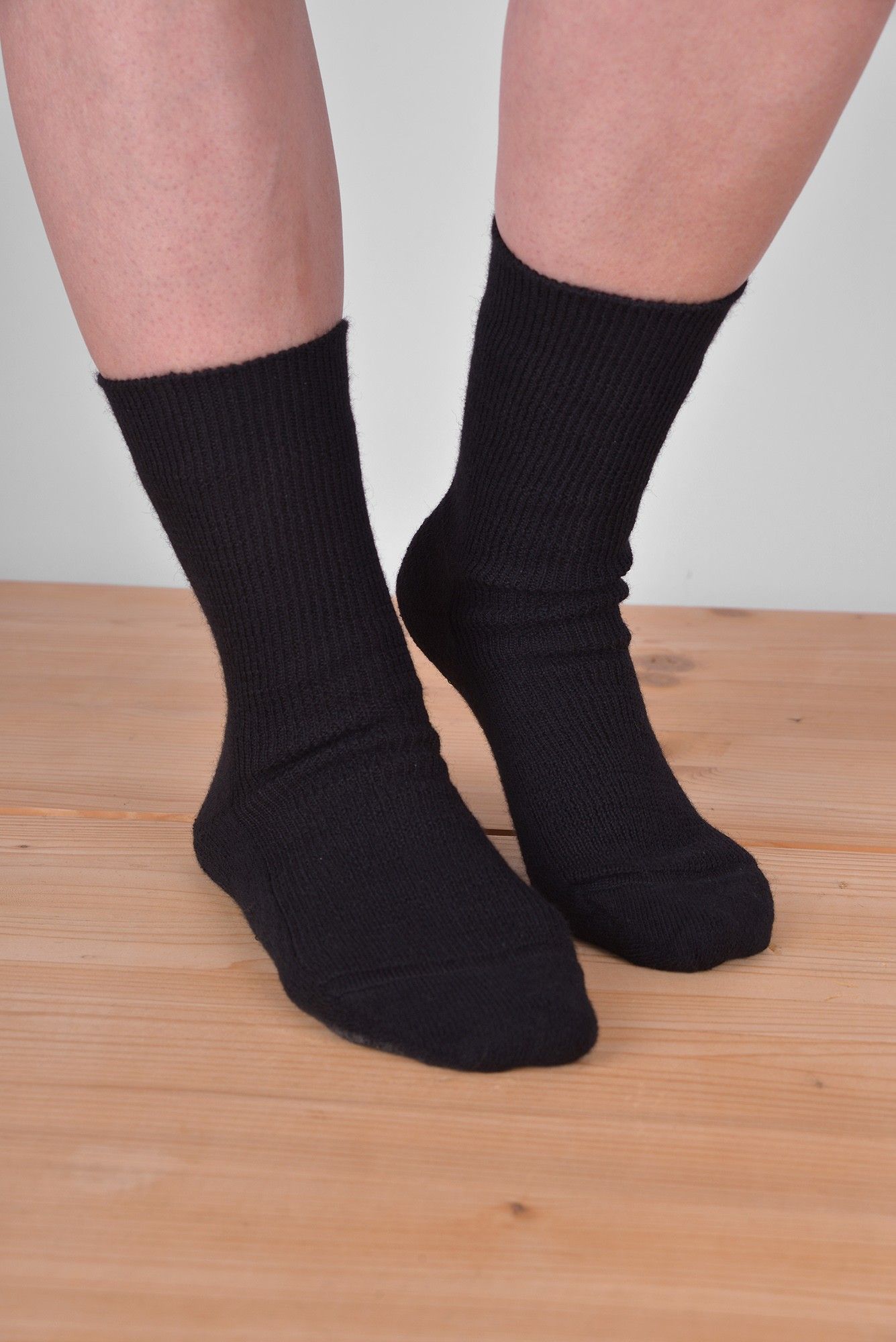 schwarze dünne Wollsocken aus bio Wolle (kbT) und bio Baumwolle (kbA) vom Finkhof an Model auf Holzboden