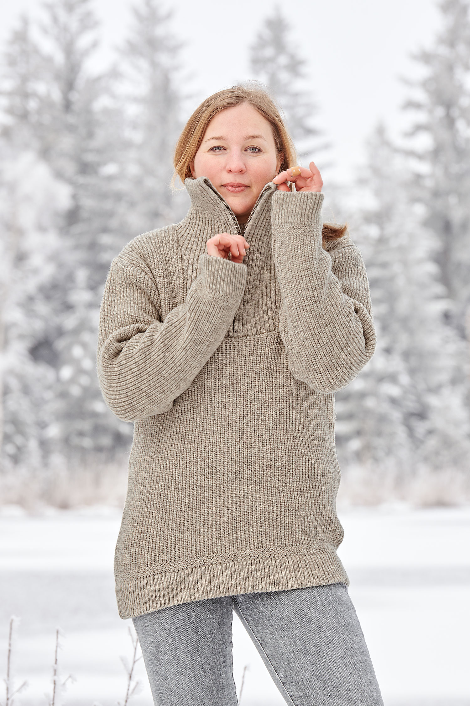 Frau in Schneelandschaft trägt grauen Finkhof Troyer aus bio Wolle (kbT) und zieht am Reißverschluss