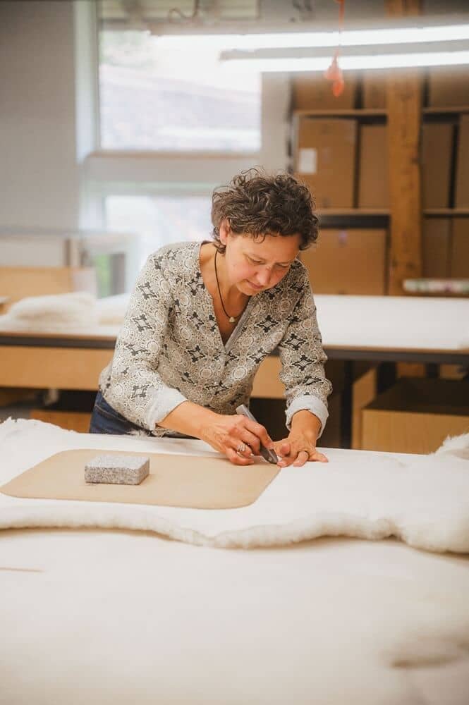 finkhof-manufakturen-fellnaeherei-1 Frau schneidet weißes Finkhof Fell mit einer Schablone aus