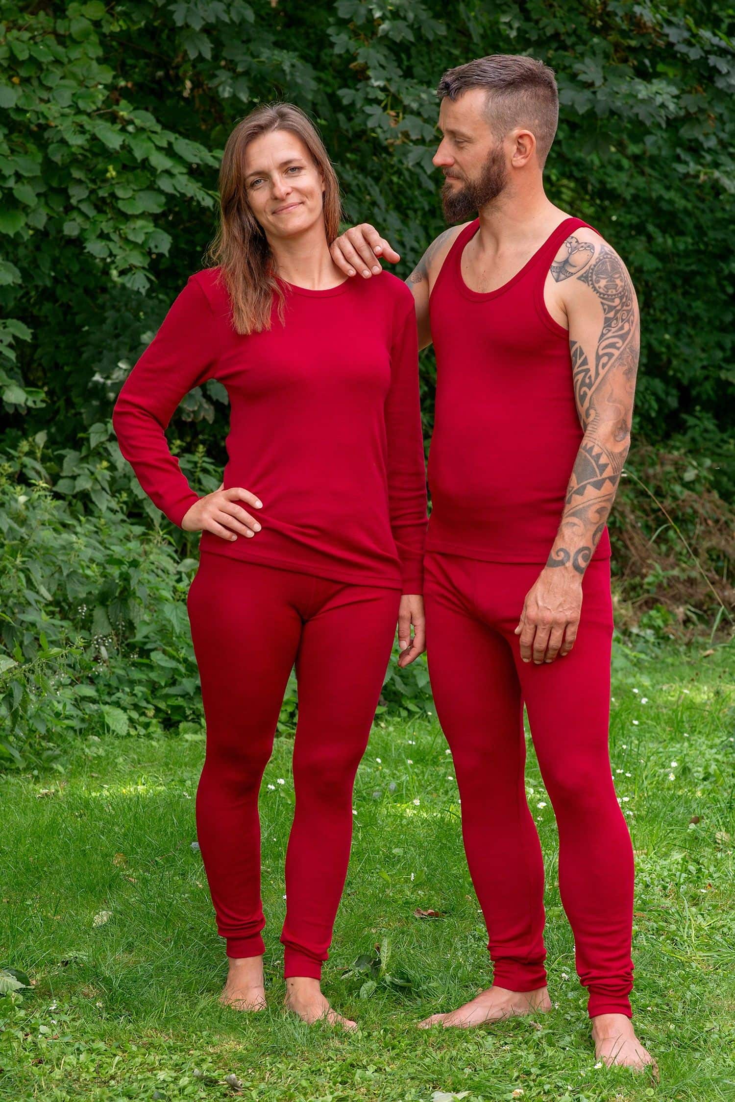Lange Wollunterhose unisex farbig aus reiner Bio-Schurwolle Mann und Frau stehen im Garten und tragen rote lange Unterhosen aus bio Wolle (kbT) mit Shirt und Top