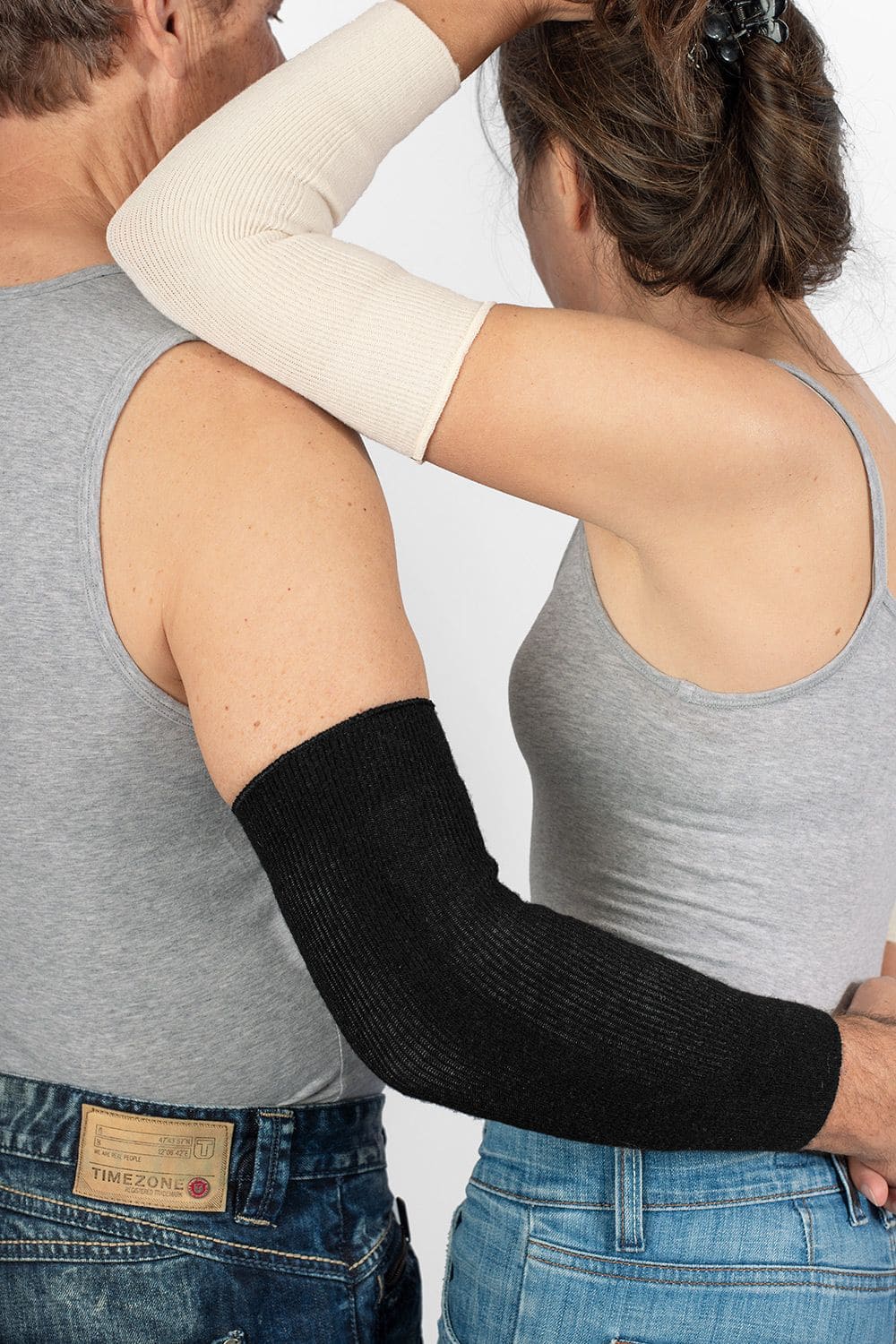 Ellbogenwärmer Mann und Frau in grauen Tops tragen naturweiße und schwarze Ellbogenwärmer aus bio Wolle (kbT), Seide, Baumwolle, Elasthan