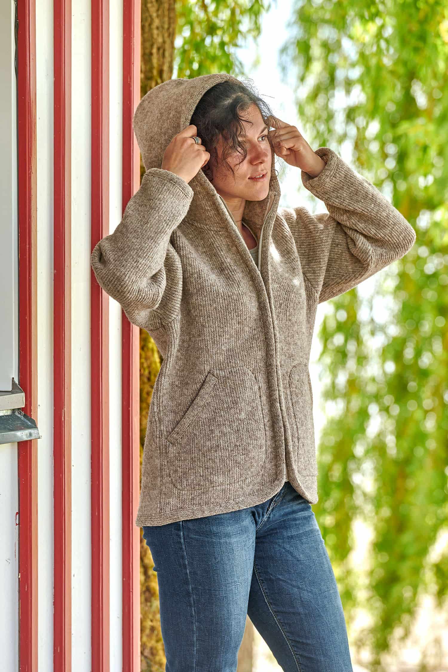 Frau setzt sich die Kapuze der grauen Finkhof Kapuzenjacke aus bio Wolle (kbT) auf