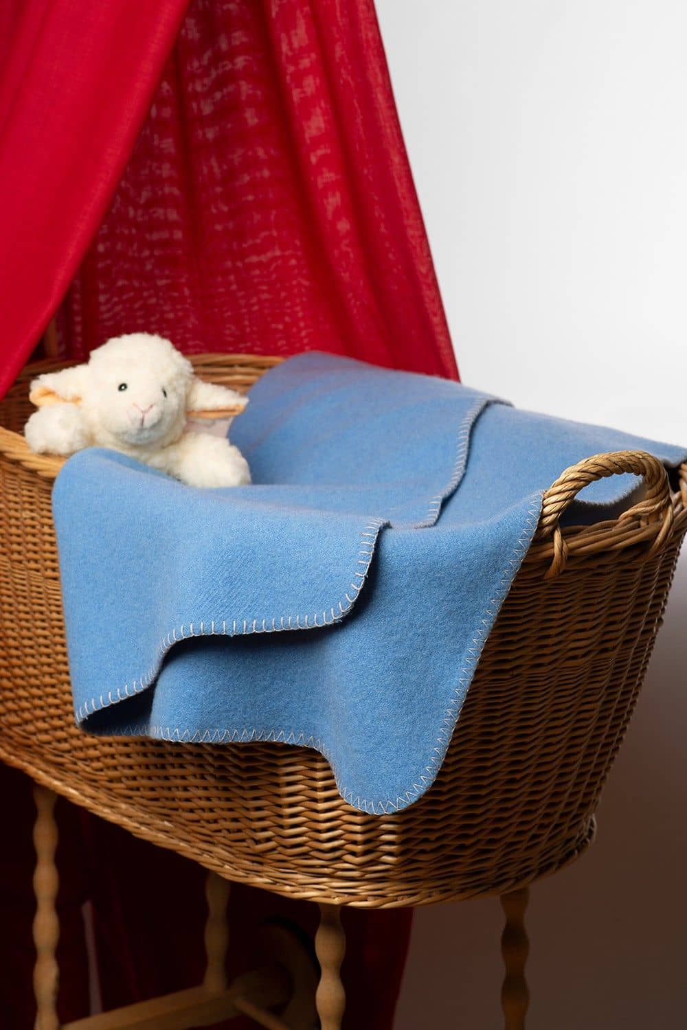 hellblaue Kinder Wolldecke aus bio Wolle (kbT) vom Finkhof liegt in einem Stubenwagen mit Kuschelschaf