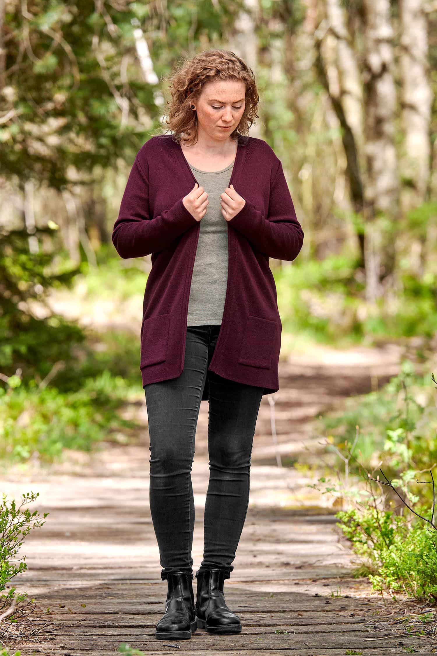 Frau mit schwarzer Jeans und einfarbigem Shirt trägt burgunderroten langen Cardigan aus bio Wolle (kbT)