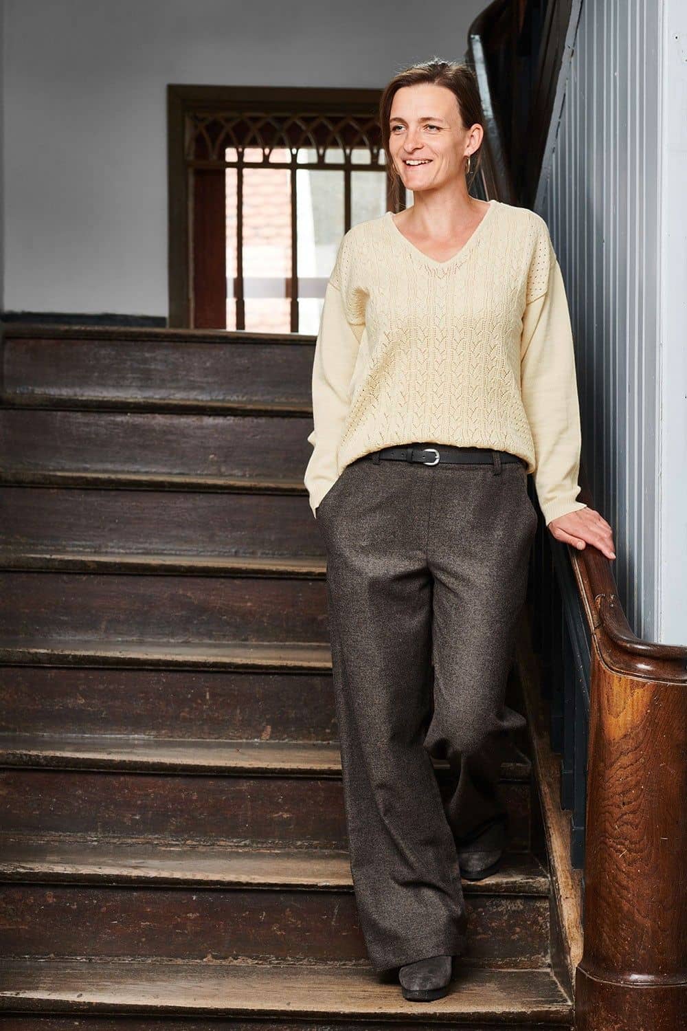 Frau geht auf Treppe und trägt weißen Pulli und eine braunmelierte Wollhose aus bio Wolle (kbT) vom Finkhof