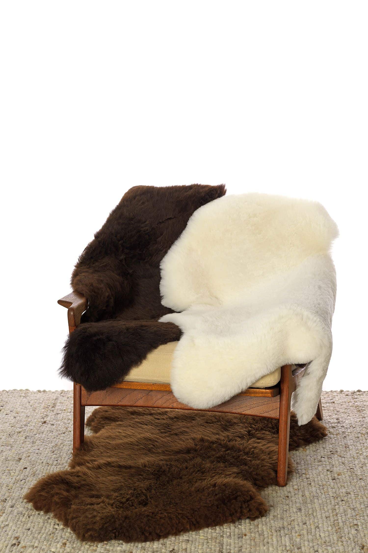 Schaffell pflanzlich gegerbte Finkhof Schaffelle in weiß und braun liegen auf einem Sessel, unter dem ein weitere Fell liegt