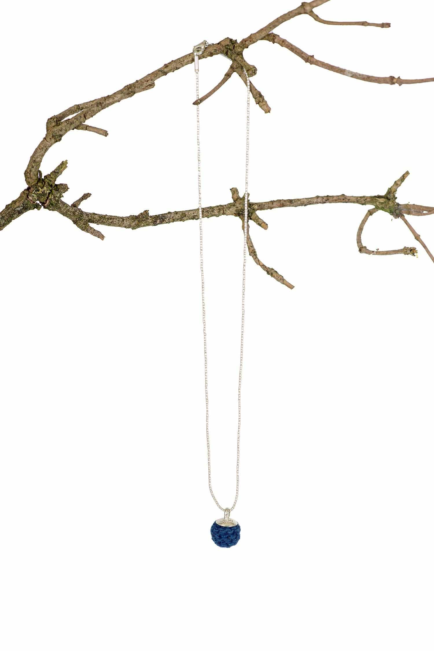 blaue handgemachte Wollperle aus pflanzengefärbter Schurwolle hängt mit einer Kette an einem Ast