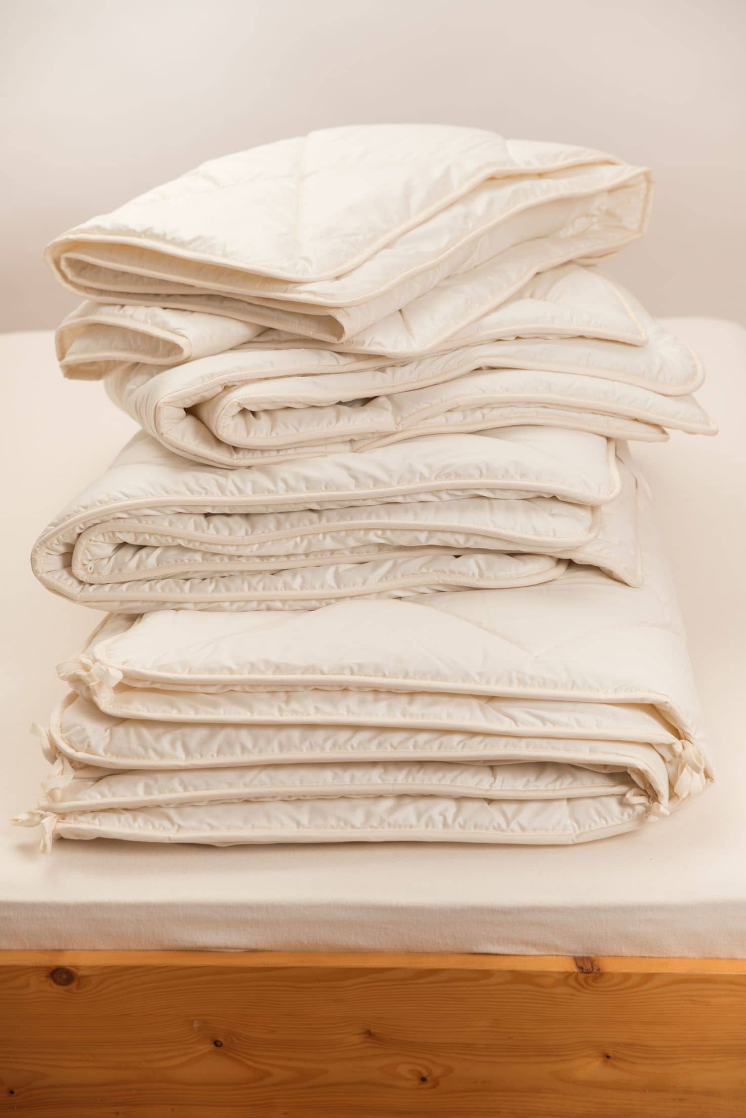 gefaltete Steppdecken sind auf braunem Holzbett aufgestappelt