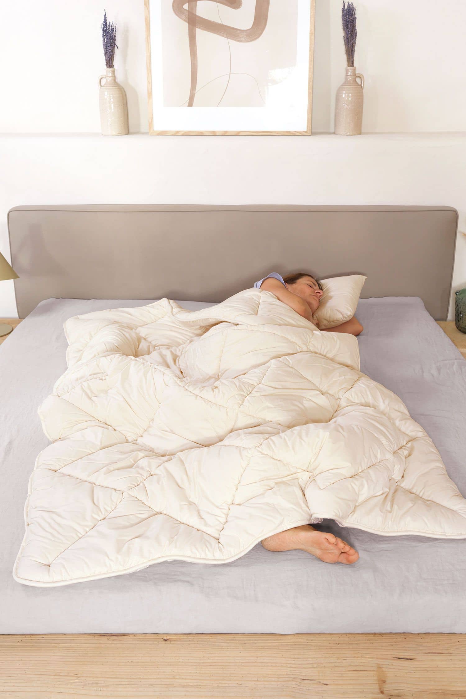 Person liegt im Bett und hat sich mit der Wintersteppdecke vom Finkhof aus bio Wolle (kbT) und bio Baumwolle (kbA) zugedeckt