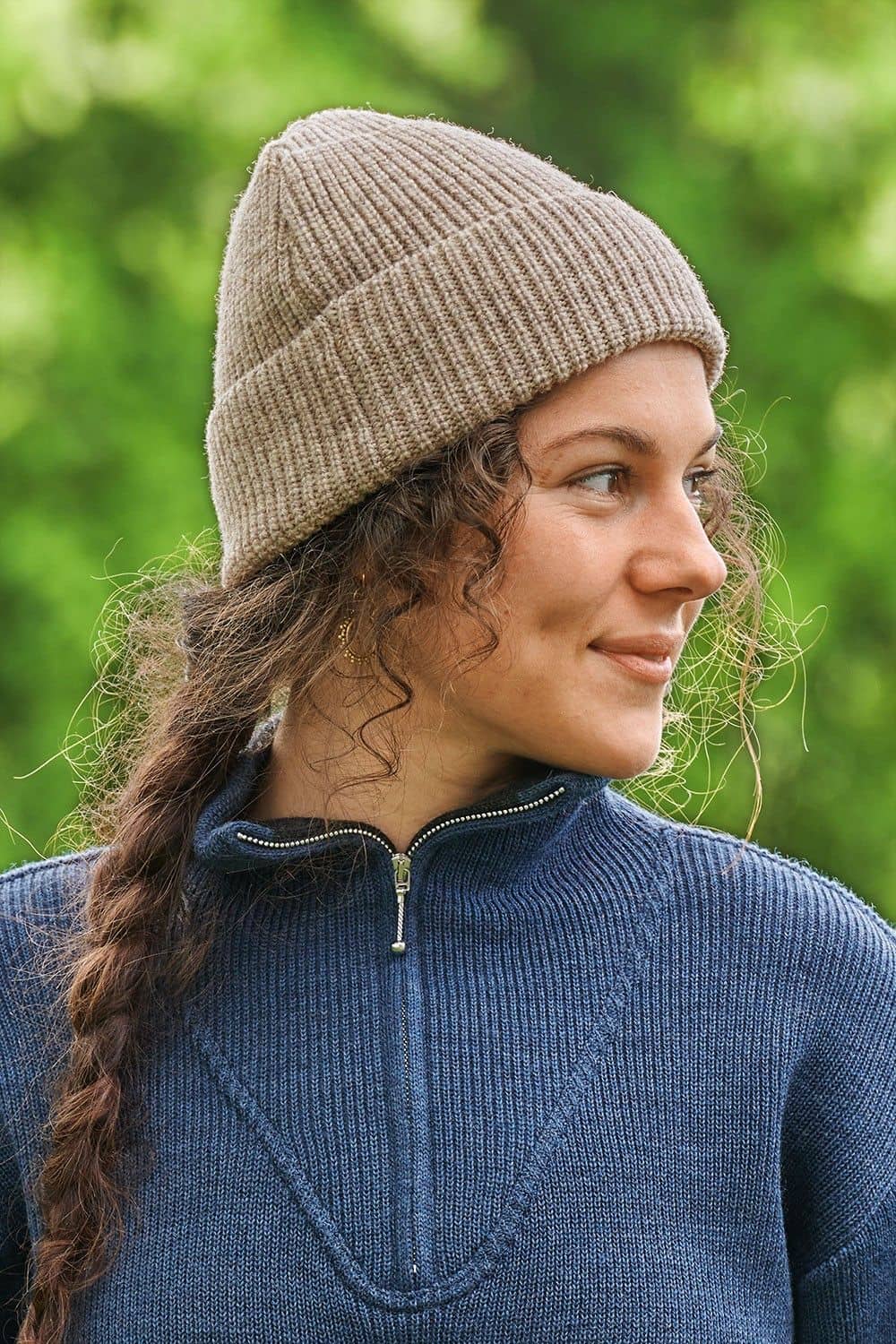 Frau mit blauem Troyer und Zopf trägt graue Finkhof Mütze aus bio Wolle (kbT)