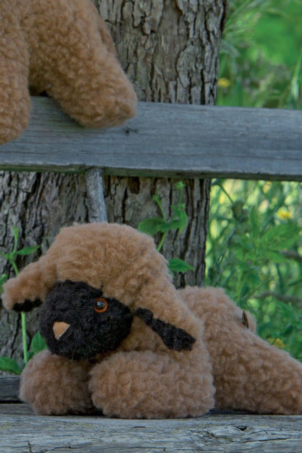 Wolltier liegendes Lamm braun braunes liegendes Lamm Kuscheltier auf Bank