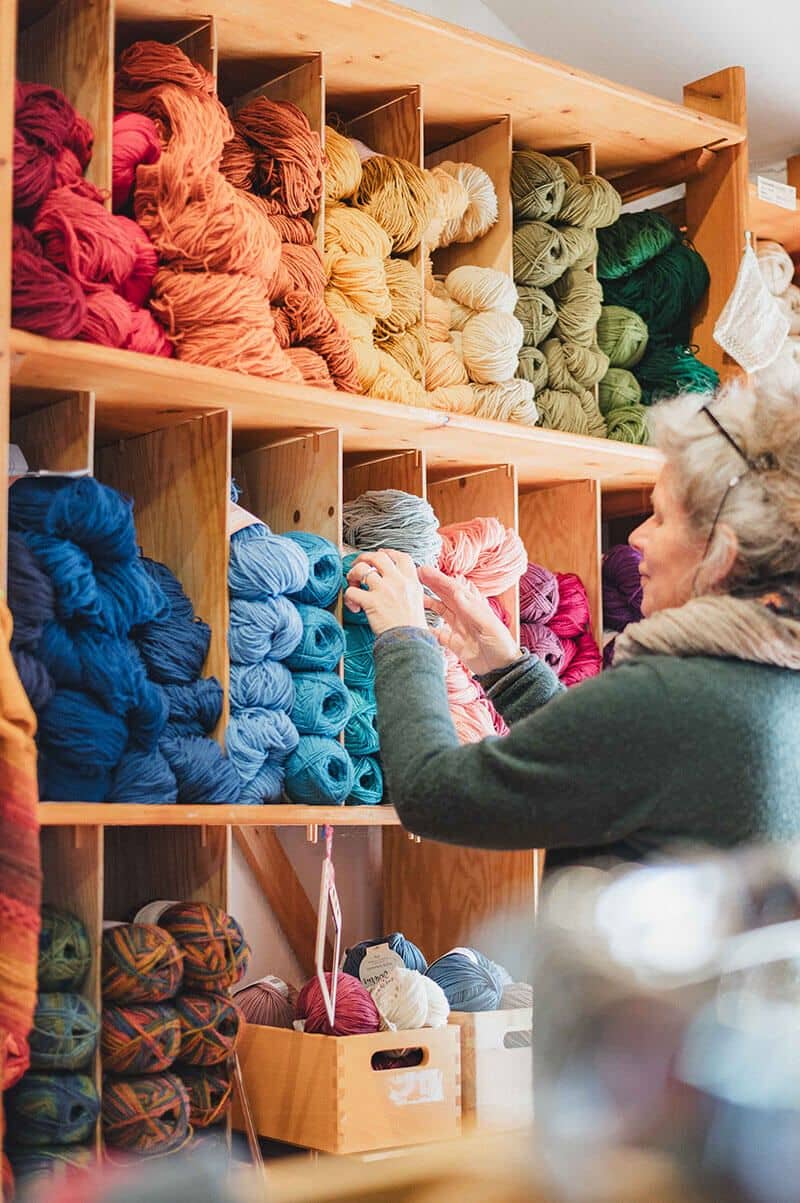 finkhof-hofladen-wollregal Frau holt Wolle aus ordentlich sortiertem Regal