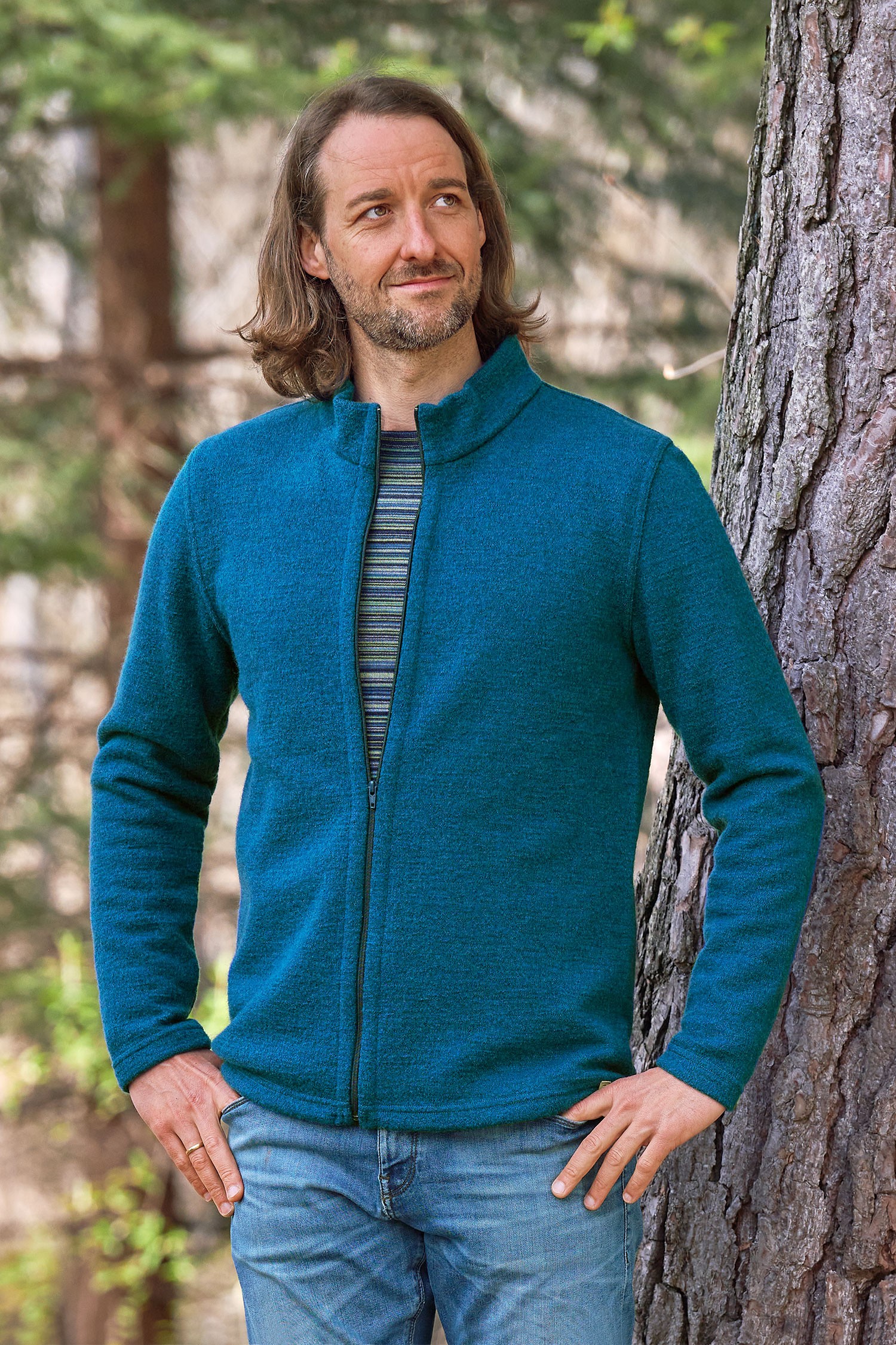 Mann steht vor einem Baum und trägt ein Streifenshirt und eine gewalkte Jacke in türkis