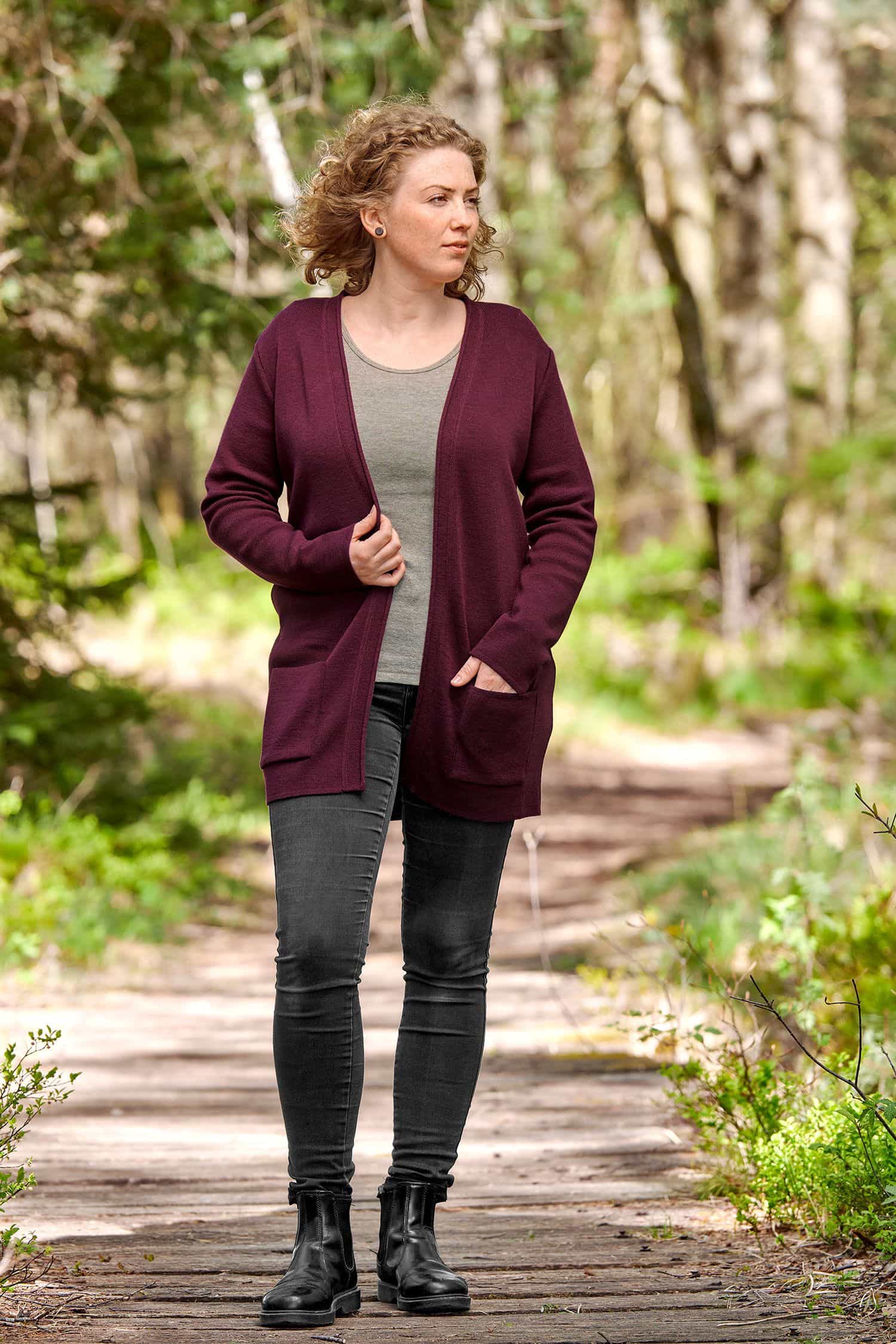 Frau mit schwarzer Jeans und einfarbigem Shirt trägt burgunderroten langen Cardigan aus bio Wolle (kbT)