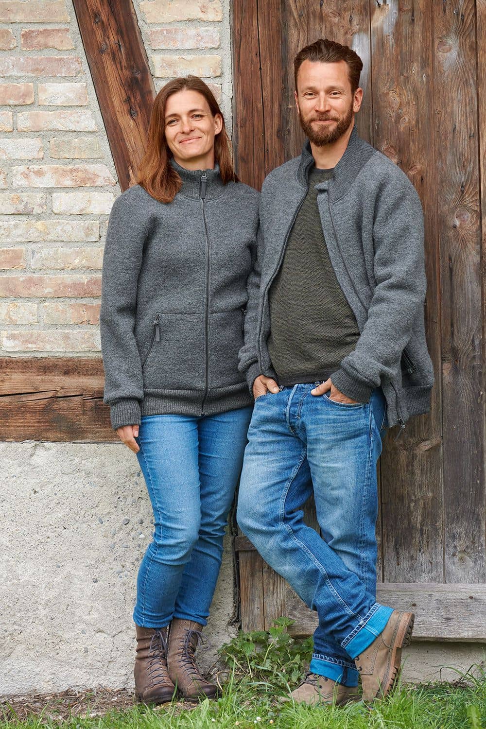 Jacke Toni Frau und Mann vor Holztor mit grauer Finkhof Jacke Toni aus bio Wolle (kbT) mit Jeans und Stiefeln