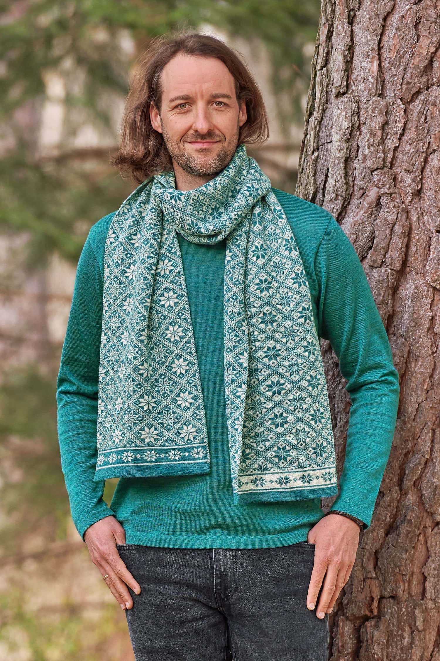 Mann vor Baum trägt türkises Shirt und Wollschal mit winterlichem Muster aus bio Wolle (kbT)