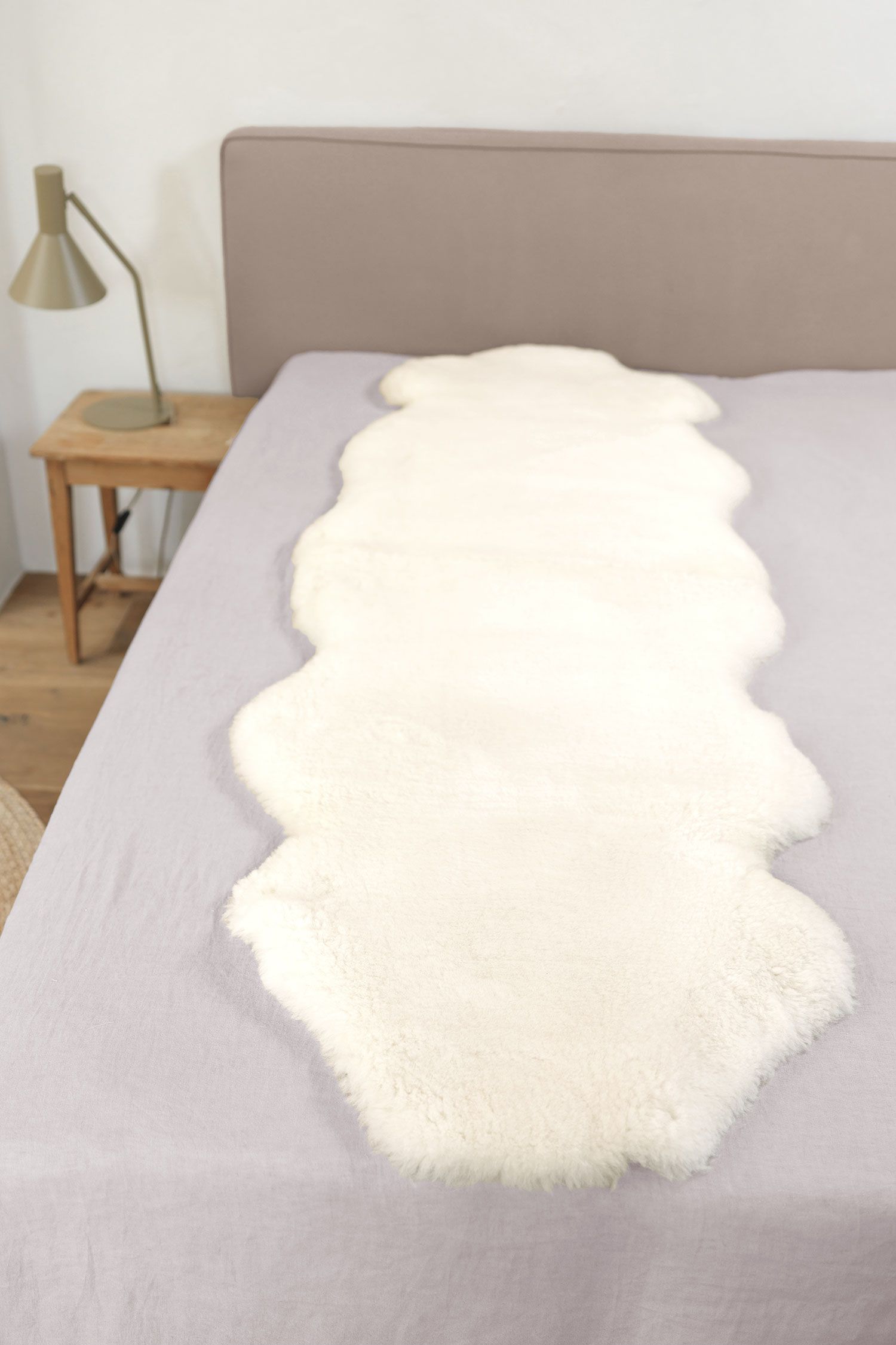 Felldecke natürliche Fellform pflanzlich, weiß 60 x 180 cm weiße pflanzlich gegerbte Felldecke in natürlicher Form aus Schaffell vom Finkhof auf grauem Bett
