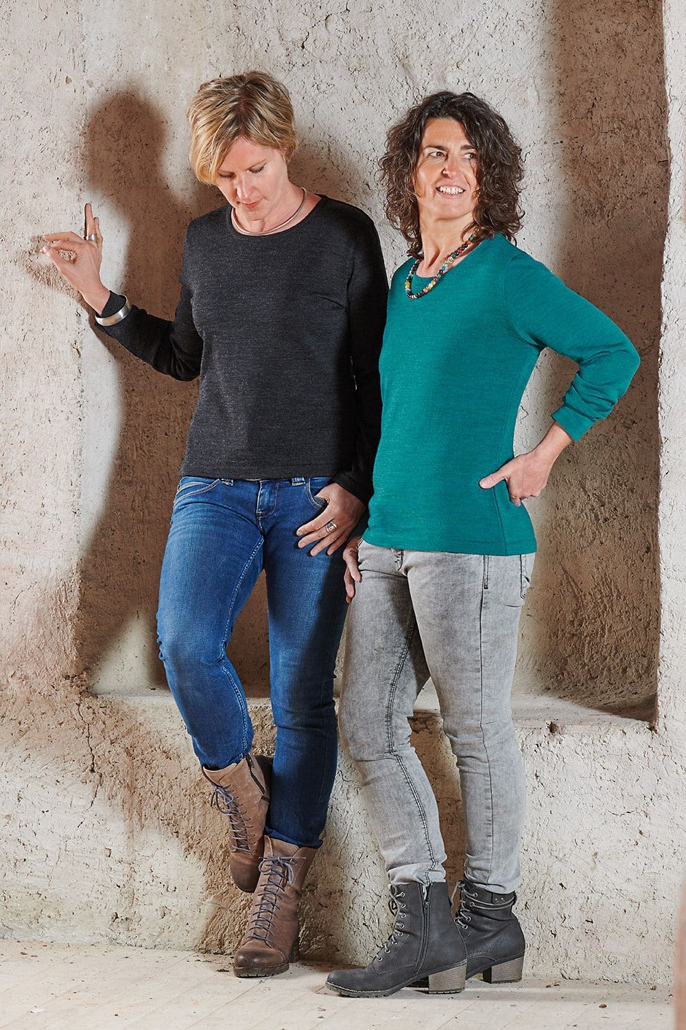 Wollshirt Frauen stehen vor Steinwand und tragen Finkhof Wollshirt aus bio Wolle (kbT) in petrol und anthrazit Jeans und Stiefeln