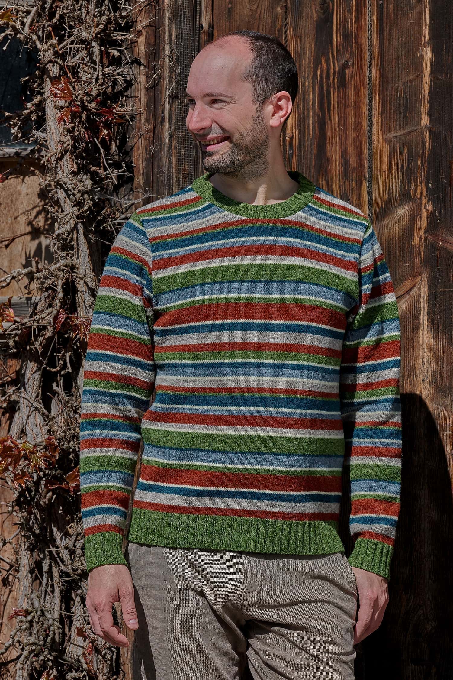 Mann trägt einen bunt gestreiften Wollpullover vom Finkhof aus Bio-Wolle und eine braune Hose