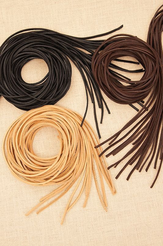 Lederbändel Lederbändel aus Rindsleder in schwarz, braun und ungefärbt aufgerollt auf beigem Untergrund