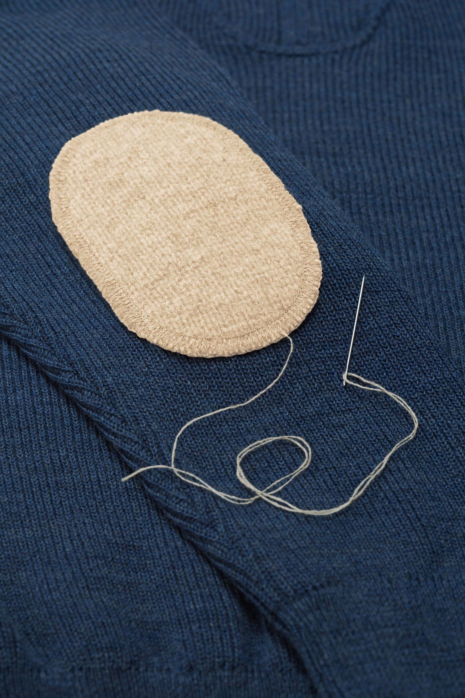 beiger Ellenbogenpatch aus bio Wolle (kbT) vom Finkhof wird auf blauen Pulli genäht