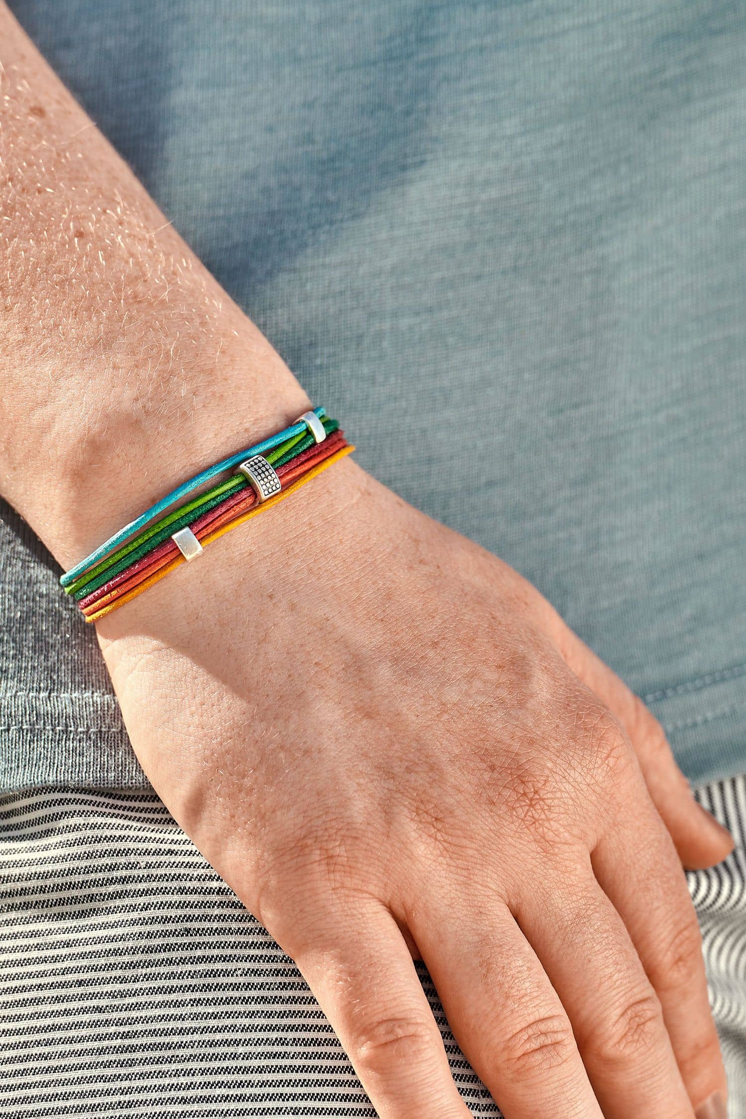 Frau mit blauem Shirt trägt kunterbuntes Lederarmband aus Rinds- und Ziegenleder mit silberfarbenem Verschluss
