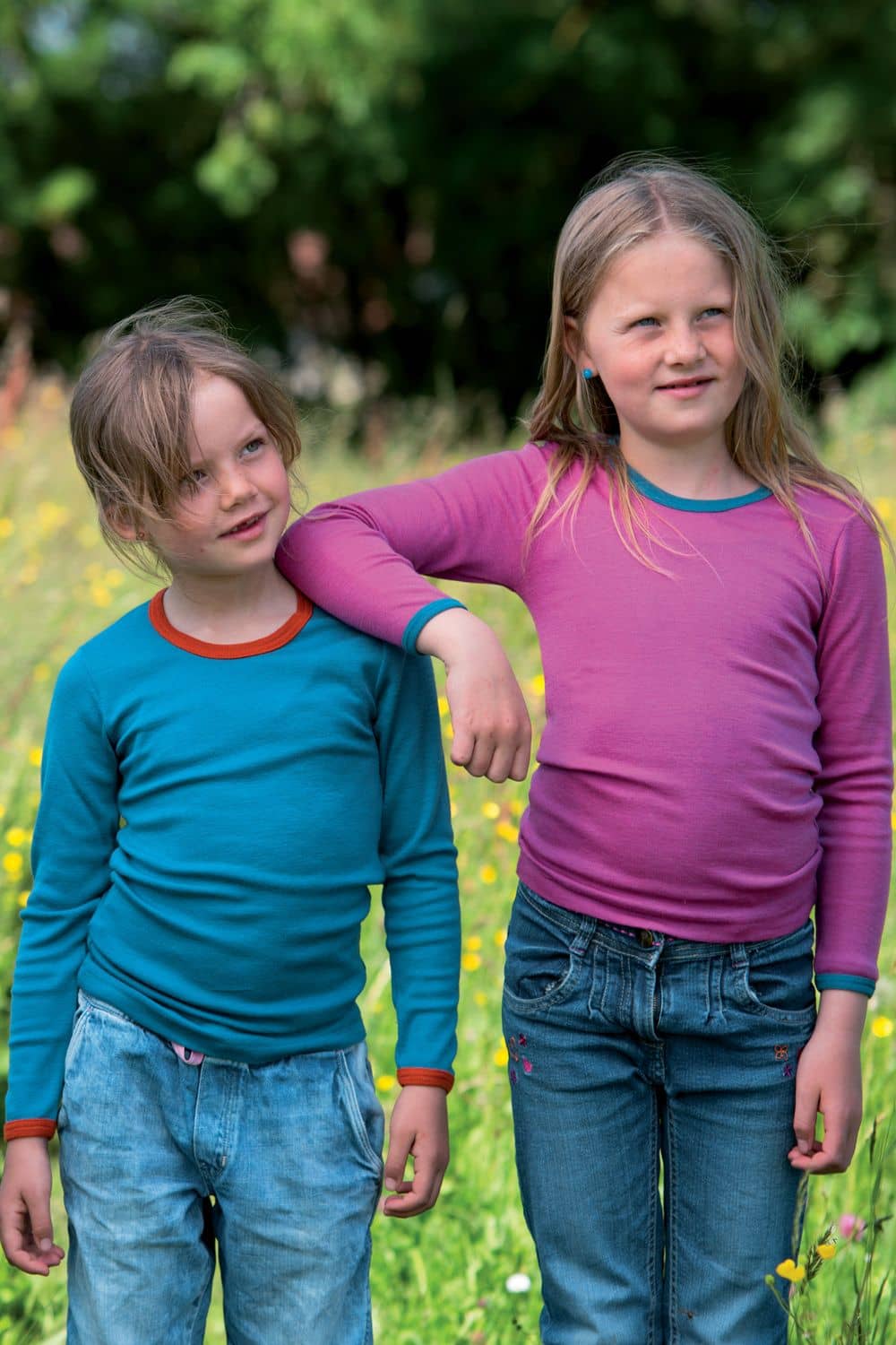 Kindershirt zweifarbig Langarm Kinder stehen auf Wiese, legen sich Arm auf und tragen dabei zweifarbige Langarmshirts aus bio Wolle (kbT) und Seide