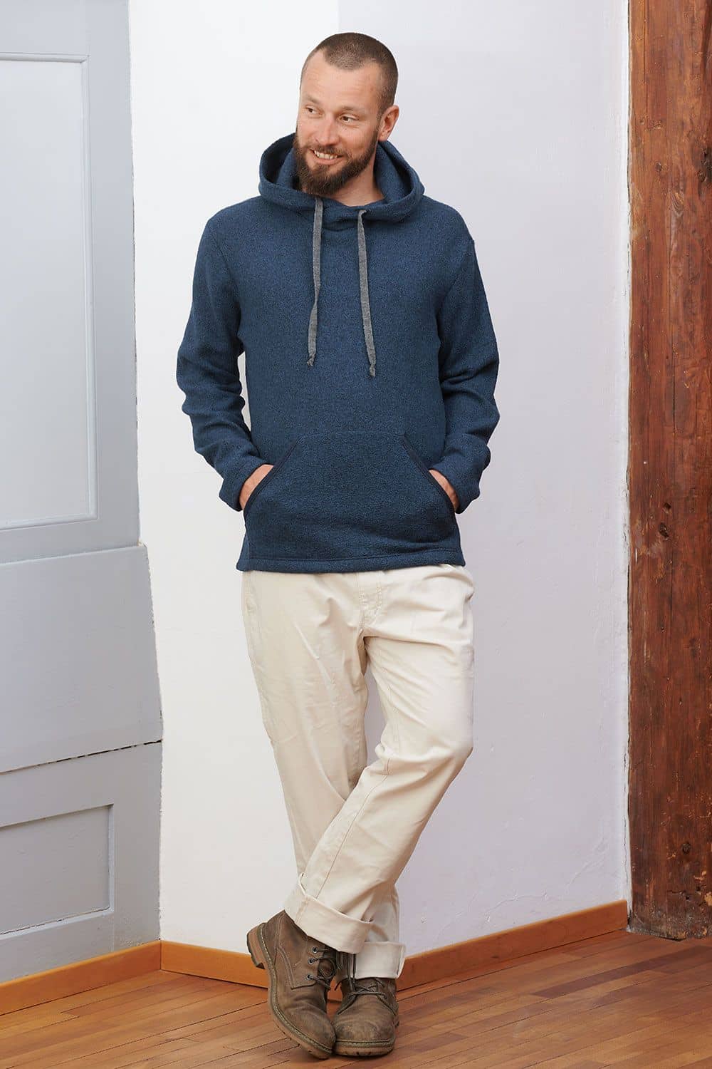Mann lehnt an Wand und trägt marineblauen Hoody aus bio Wolle (kbT) mit beiger Jeans