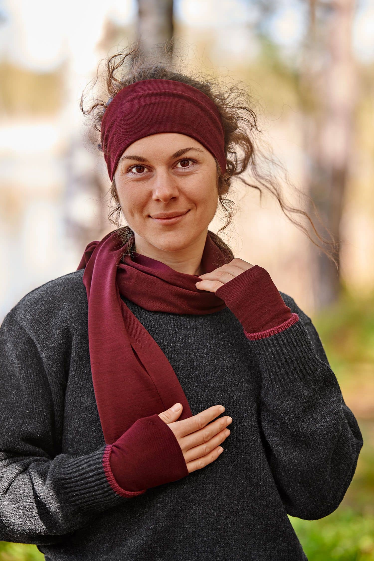 Frau mit grauem Pulli trägt bordeauxrote Pulswärmer aus bio Wolle (kbT) und Seide mit Schal und Stirnband