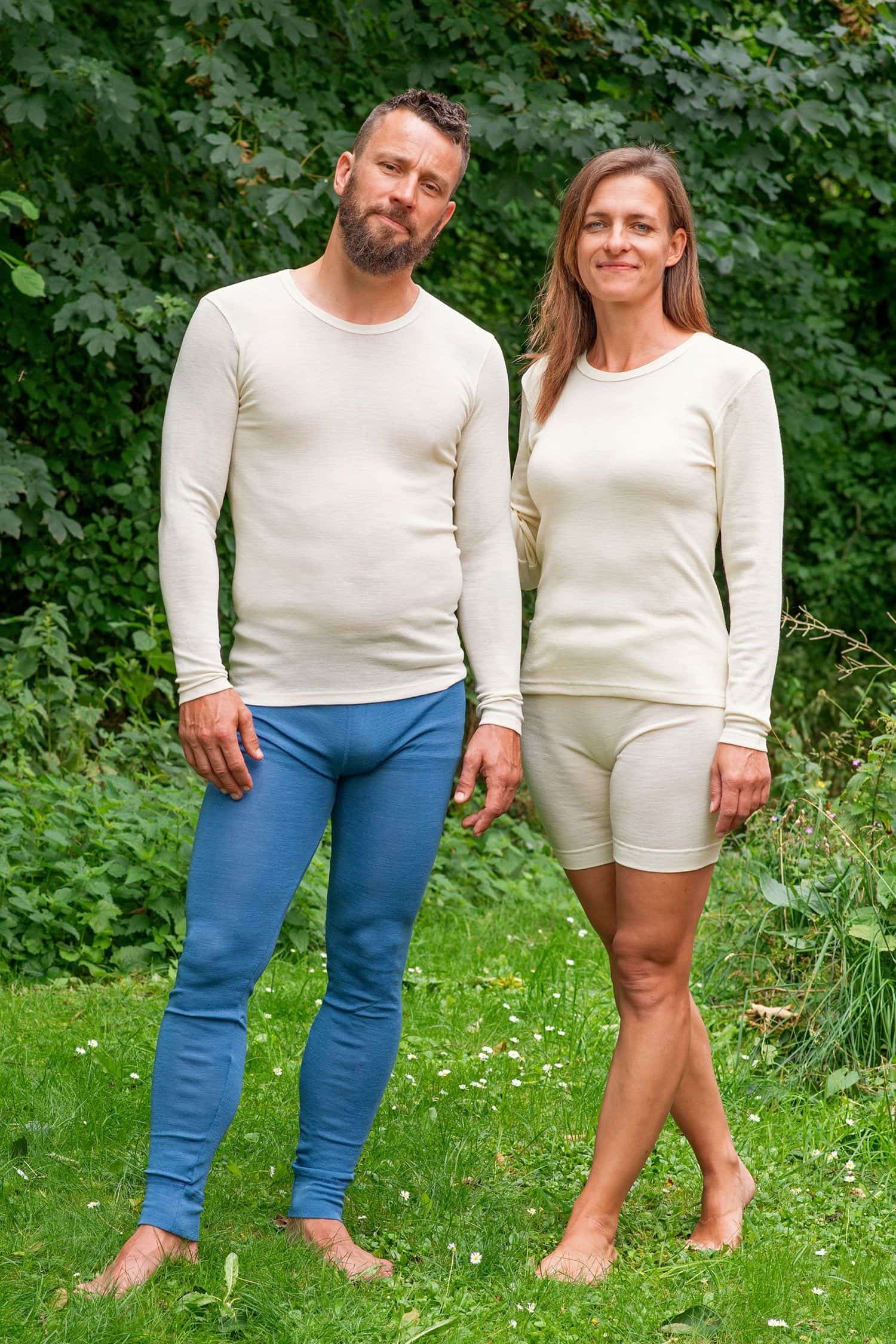 Mann und Frau tragen langärmelige Wollhemden in naturweiß aus bio Wolle (kbT) mit blauer und weißer Hose im Garten