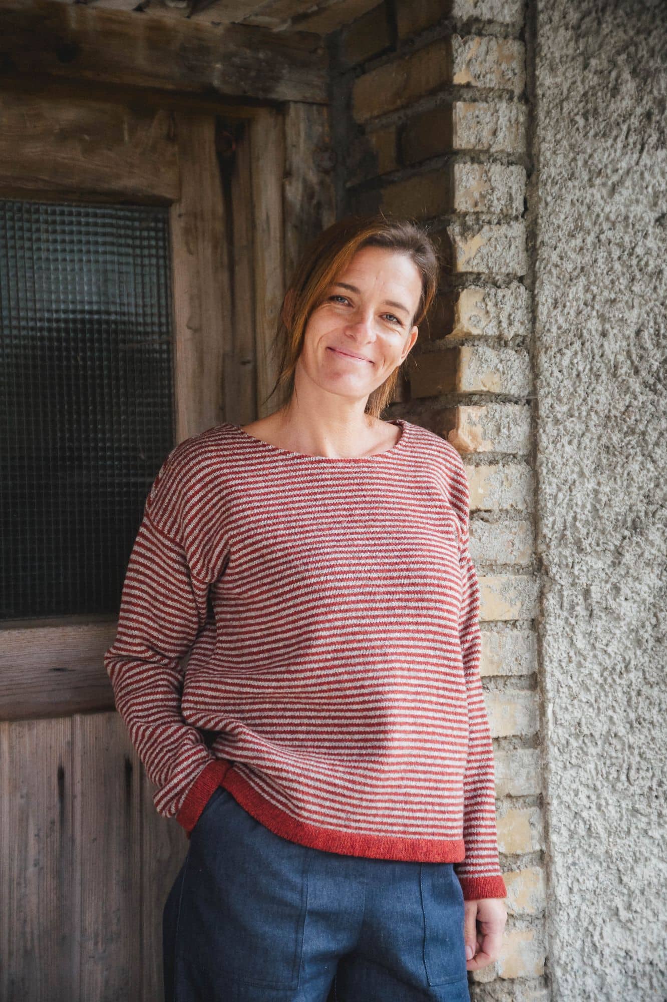 Finkhof-Damen-Ringelpulli siena Gr. M Frau mit blauer Stoffhose trägt roten Ringelpulli aus bio Wolle (kbT) vom Finkhof