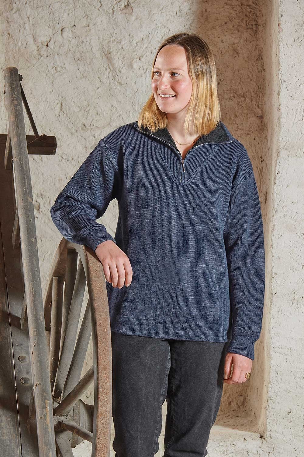 Frau lehnt sich auf altes Holzrad und trägt einen blauen Troyer aus bio Wolle (kbT) vom Finkhof