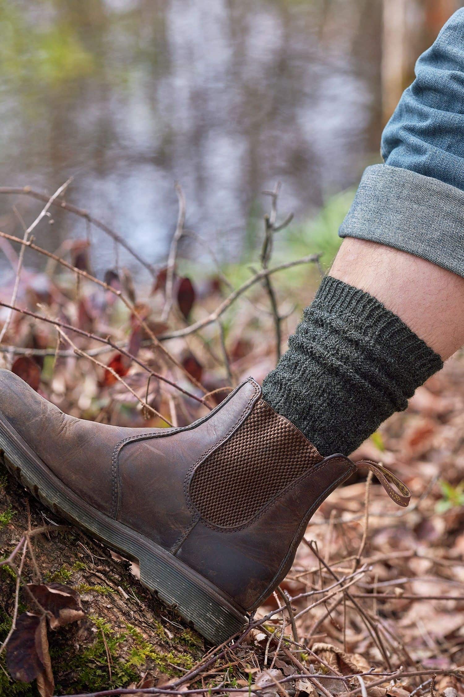 Person stellt Fuß auf Moos und trägt dunkelgraue Struktursocken aus bio Wolle (kbT) vom Finkhof mit braunen Stiefeln