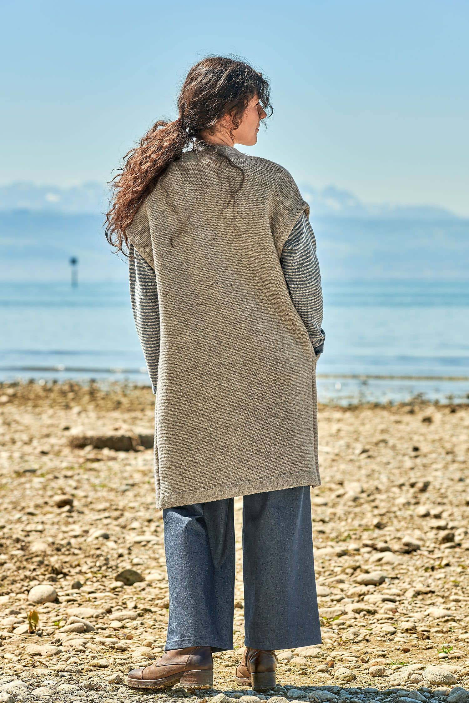 Rückansicht von Frau mit weiter Hose und grauer langer Strickweste vom Finkhof aus bio Merinowolle (kbT)