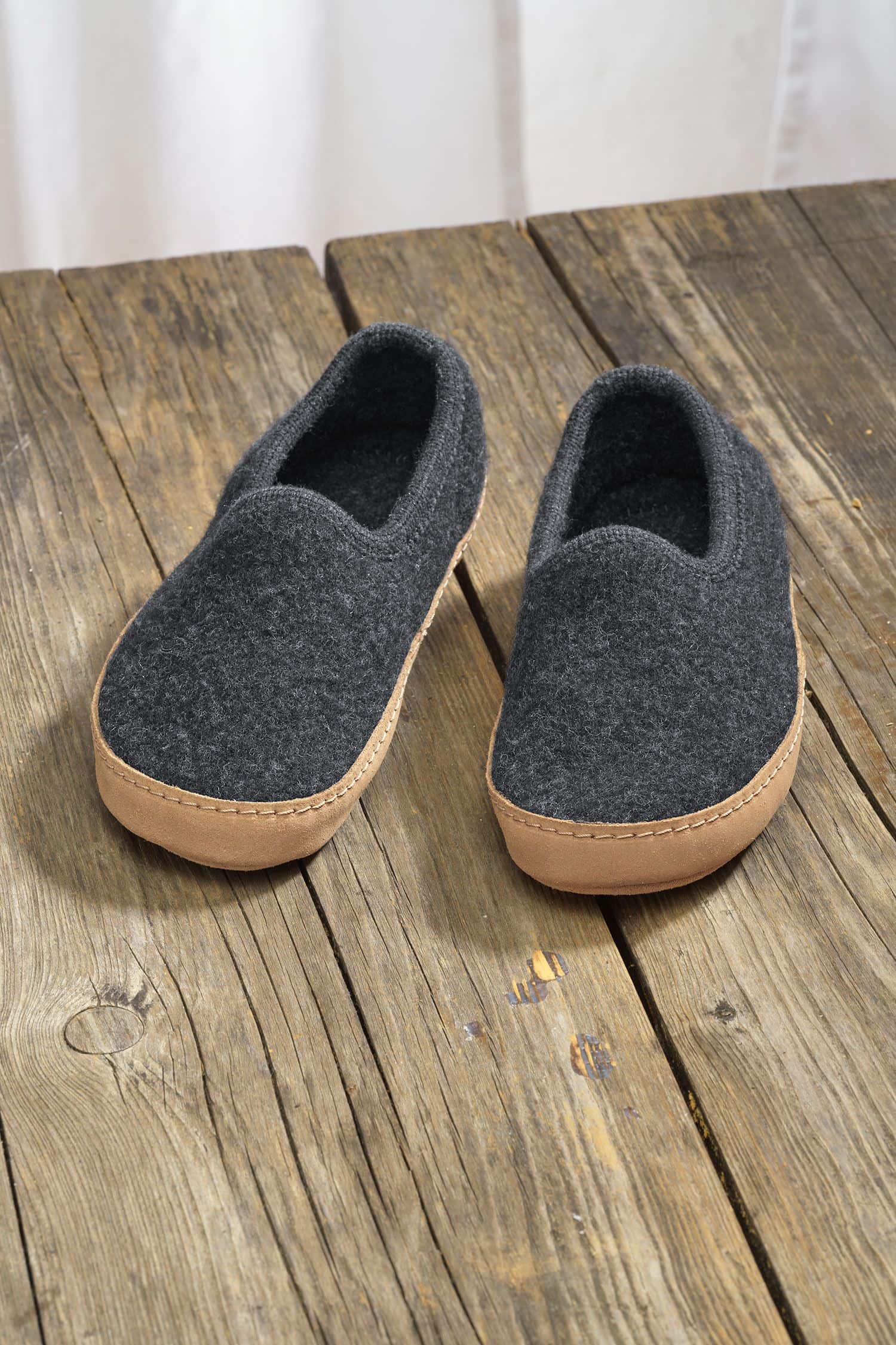 Paar dunkelgraue Finkhof Hausschuhe aus bio Wolle (kbT) und einer Sohle aus pflanzlich gegerbtem Rindsleder auf Holzboden